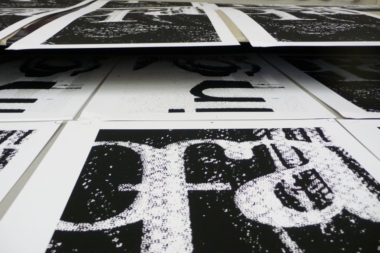 Schwarz-weiße Typografie-Drucke liegen in Reihen auf einer Arbeitsfläche und zeigen vergrößerte Buchstaben und Strukturen.