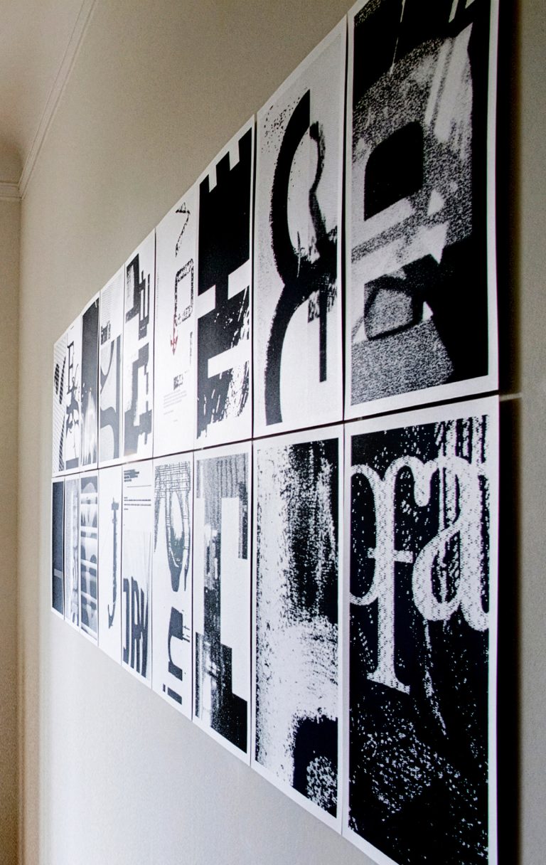 An einer Wand montierte Serie schwarz-weißer Drucke mit abstrahierten Buchstaben und typografischen Fragmenten.