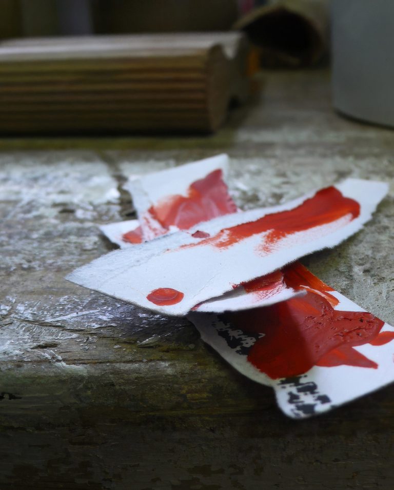 Papierreste mit roter Druckfarbe liegen auf einer Werkbank im Atelier.