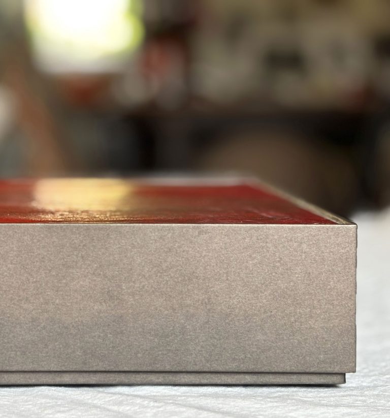 Geschlossene dunkelgraue Archivbox mit rotem Einleger auf einem Tisch, der Hintergrund ist unscharf.
